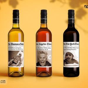 May include: Three wine bottles with newspaper-themed labels. The labels read "The Boston Globe," "Los Angeles Times," and "The New York Times." Each bottle has a different colored wine and a black cap. The background is yellow.