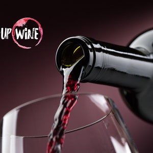 May include: A bottle of red wine being poured into a clear glass. The wine is a deep red color and the glass is clear. The text "PICK-UP WINE" is visible in the background.