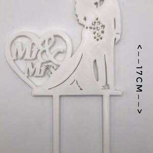 Pu&ograve; includere: Topper per torta in plastica bianca con una silhouette di sposa e sposo con un cuore che dice "Mr & Mrs". Il topper &egrave; alto 17 cm e largo 10 cm.