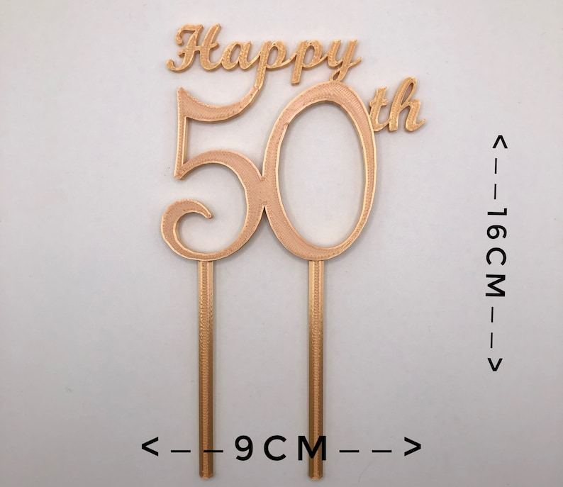 May include: Gold-colored cake topper with the words "Happy 50th" and the number 50. The topper is 16 cm tall and 9 cm wide.