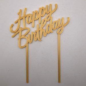 May include: Gold cake topper with the words "Happy Birthday" in a cursive font.
