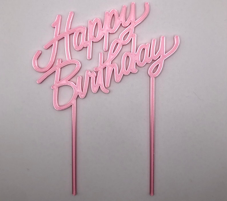 May include: Pink cake topper with the words "Happy Birthday" in a cursive font.
