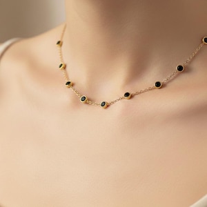 May include: A delicate gold necklace featuring small, round black gemstones evenly spaced along the chain. The necklace is displayed against a neutral background, highlighting the jewelry's simple elegance and design.