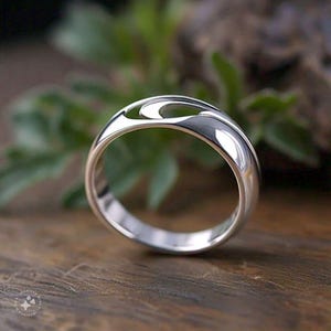 May include: A silver ring with a unique, abstract design featuring a cutout shape. The ring is smooth and polished, with a contemporary style.