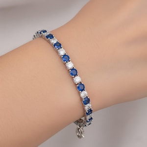 Può includere: Un bracciale d'argento con pietre preziose blu e bianche rotonde alternate. Il bracciale è assicurato con una chiusura. Le pietre sono incastonate vicine, creando una linea continua di brillantezza.