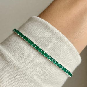 Op de afbeelding: Een zilveren armband met een rij vierkante smaragdgroene stenen.
