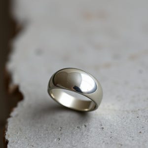 May include: A silver ring with a rounded, domed top. The ring is smooth and polished, reflecting light.