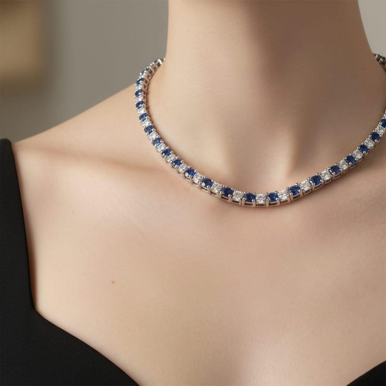 May include: A silver necklace featuring alternating blue and white gemstones. The necklace is worn around the neck. The gemstones are square-cut and set closely together, creating a continuous line of sparkle. The necklace is a classic design.