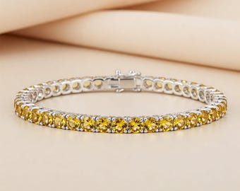 May include: A tennis bracelet featuring a row of round, yellow gemstones set in a silver-toned metal. The bracelet is secured with a clasp. The gemstones are evenly spaced and reflect light, creating a sparkling effect.