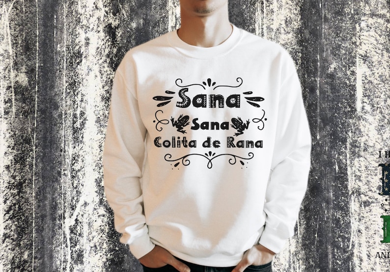 Op de afbeelding: Wit sweatshirt met zwarte tekst en kikkerillustraties. De tekst luidt "Sana Sana Colita de Rana".