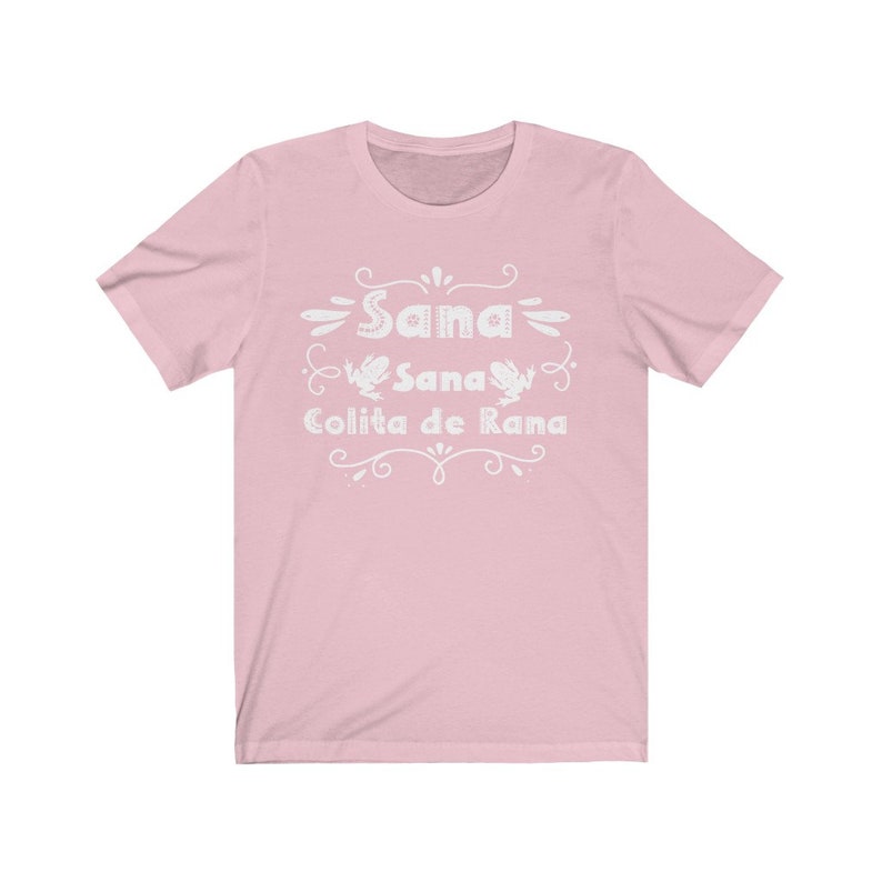 Op de afbeelding: Roze T-shirt met een wit grafisch ontwerp met de tekst "Sana Sana Colita de Rana" en twee kikkerillustraties.