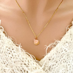 May include: A gold chain necklace with a small, round pendant featuring a pink crystal. The pendant is attached to the chain with a delicate wire.