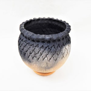 May include: A black and white ceramic pot with a textured surface. The pot has a wide, round base and a narrow opening.