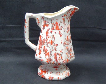 May include: White ceramic pitcher with a red and gray splatter pattern. The pitcher has a wide mouth and a handle.