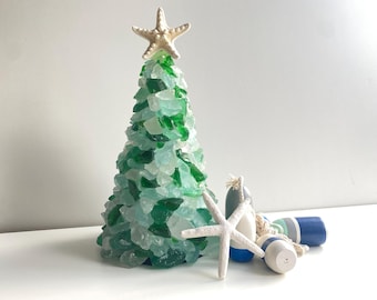 May include: A green and blue glass sea glass Christmas tree with a white starfish on top. The tree is surrounded by white starfish and blue and white nautical buoys.