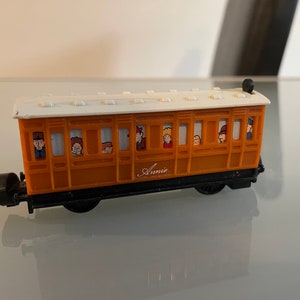 May include: A brown and white toy train carriage with the name "Annie" printed on the side. The carriage has windows with cartoon figures looking out of them.