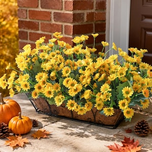 May include: A rectangular black wire planter filled with artificial yellow daisy flowers and green leaves. The planter has a textured brown liner and is displayed with two orange pumpkins, pinecones, and fallen autumn leaves nearby.
