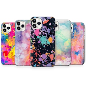 Puede incluir: Cinco fundas de teléfono diferentes con diseños de salpicaduras de pintura de colores. Las fundas son todas transparentes y muestran el objetivo de la cámara del teléfono. Los diseños incluyen un fondo negro con salpicaduras de pintura de colores, un fondo rosa con salpicaduras de pintura de colores, un fondo azul claro con nubes de acuarela, un fondo rosa claro con nubes de acuarela y un fondo naranja claro con nubes de acuarela.