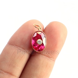 May include: A gold pendant with a red oval gemstone and a small white diamond in the center.