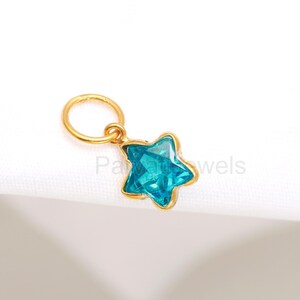 May include: A gold charm with a blue star-shaped crystal. The charm has a small loop at the top for attaching to a necklace or bracelet.