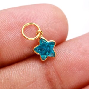 May include: A gold charm with a blue star-shaped crystal. The charm has a small loop at the top for attaching to a necklace or bracelet.