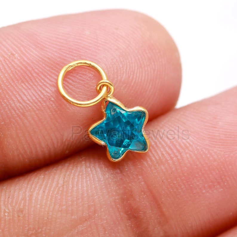 May include: A gold charm with a blue star-shaped crystal. The charm has a small loop at the top for attaching to a necklace or bracelet.