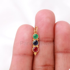 May include: Gold pendant featuring three round gemstones. The top gemstone is green, the middle gemstone is blue, and the bottom gemstone is red.