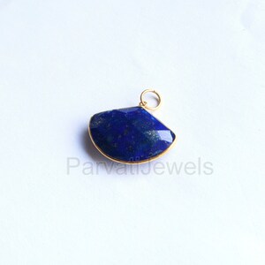 May include: A gold-toned pendant featuring a large, dark blue lapis lazuli gemstone with a fan-shaped cut. The gemstone is set in a gold-toned bezel.