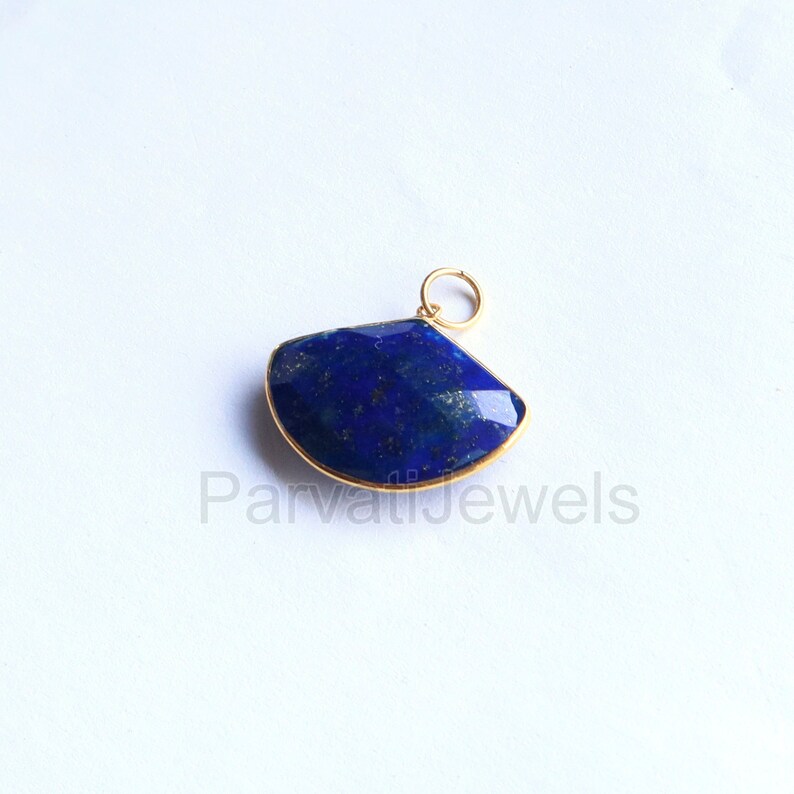 May include: A gold-toned pendant featuring a large, dark blue lapis lazuli gemstone with a fan-shaped cut. The gemstone is set in a gold-toned bezel.