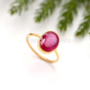 May include: A gold ring featuring a large, oval-shaped ruby gemstone. The ruby is a deep red colour and has a faceted cut.