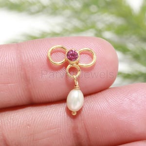 May include: Gold nose ring with a pink gemstone and a white pearl dangle.