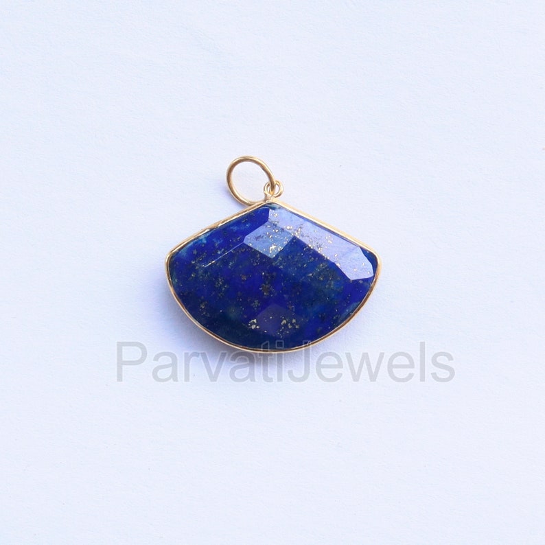 May include: A gold pendant featuring a large, faceted, blue lapis lazuli stone. The stone is set in a gold frame and has a fan shape.
