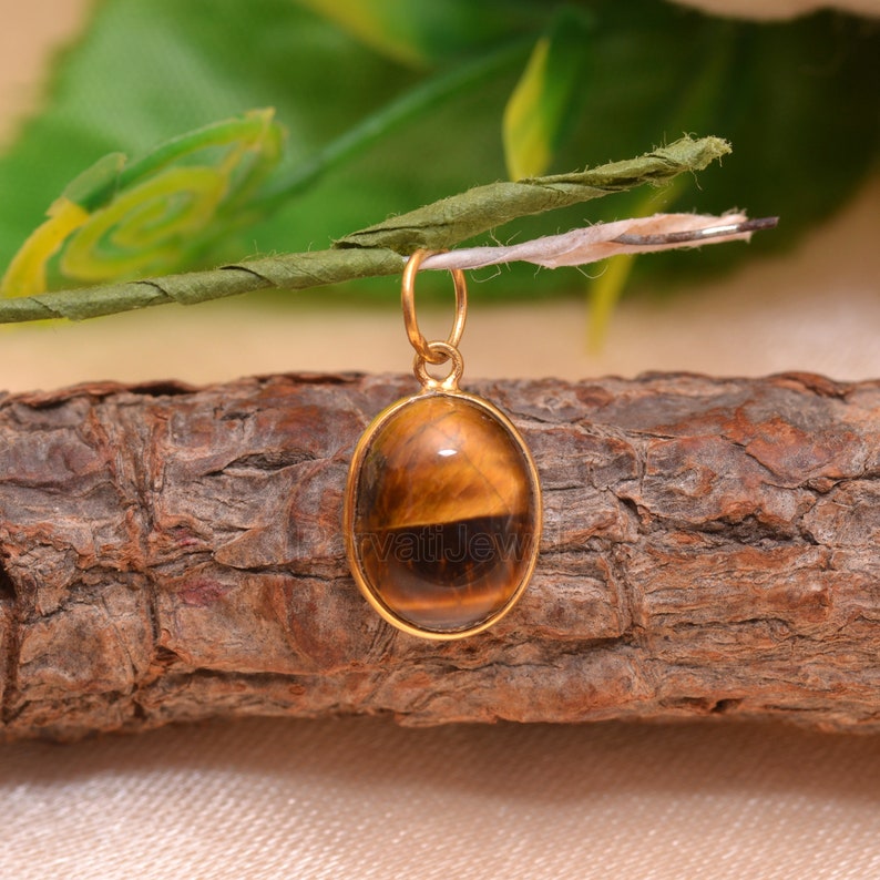 May include: Gold pendant featuring a brown and gold oval tiger's eye gemstone.