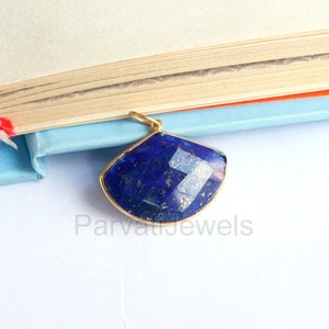 May include: A gold pendant featuring a large, faceted, dark blue lapis lazuli gemstone. The gemstone is set in a gold frame and has a slightly curved shape.