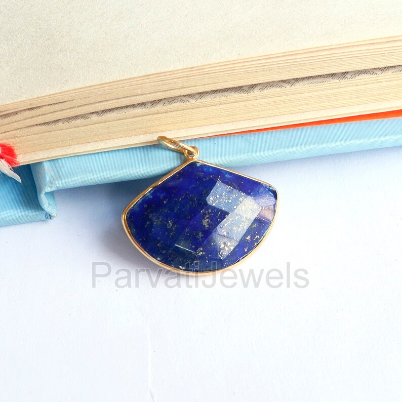 May include: A gold pendant featuring a large, faceted, dark blue lapis lazuli gemstone. The gemstone is set in a gold frame and has a slightly curved shape.