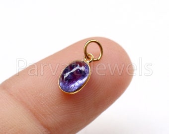 May include: A small gold pendant with a purple oval gemstone. The pendant has a loop for attaching to a chain.