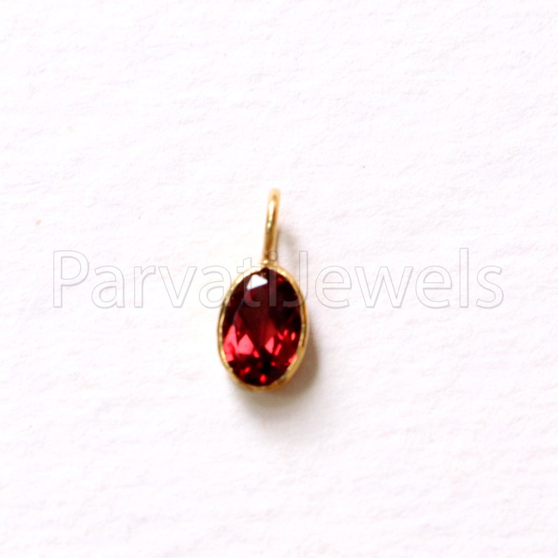 May include: A red gemstone pendant with a gold setting. The pendant is oval shaped and has a smooth, polished finish.