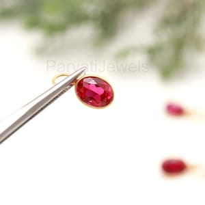Op de afbeelding: Een close-up van een rode edelsteen oorbel met een gouden zetting. De oorbel wordt vastgehouden door een pincet.