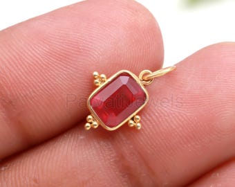 May include: A gold-colored pendant with a rectangular, faceted, red gemstone. The gemstone is set in a gold frame with decorative gold accents. The pendant has a small loop for attaching to a chain. The text "Pavati jewels" is visible.