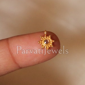 Puede incluir: Anillo de nariz de oro con una pequeña piedra preciosa transparente en el centro. El anillo tiene forma de estrella con pequeñas cuentas alrededor del borde. El anillo está sostenido por un dedo.