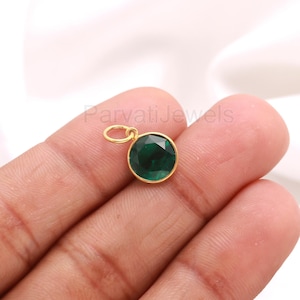 May include: A gold pendant with a round, faceted, emerald-green gemstone. The pendant has a small loop at the top for attaching to a chain. The gemstone is set in a gold bezel.