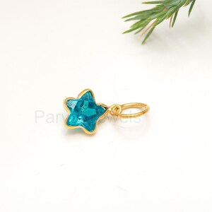 May include: A gold star charm with a blue gemstone. The charm has a small loop for attaching to a necklace or bracelet.