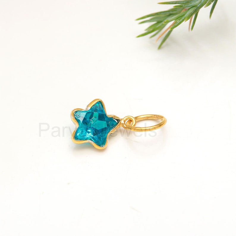 May include: A gold star charm with a blue gemstone. The charm has a small loop for attaching to a necklace or bracelet.