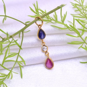 May include: A gold pendant with three teardrop-shaped gemstones. The top gemstone is blue, the middle is white, and the bottom is pink.