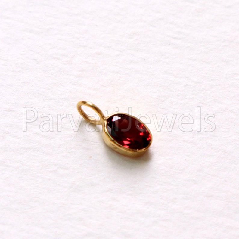 May include: A small gold pendant with a red oval gemstone.