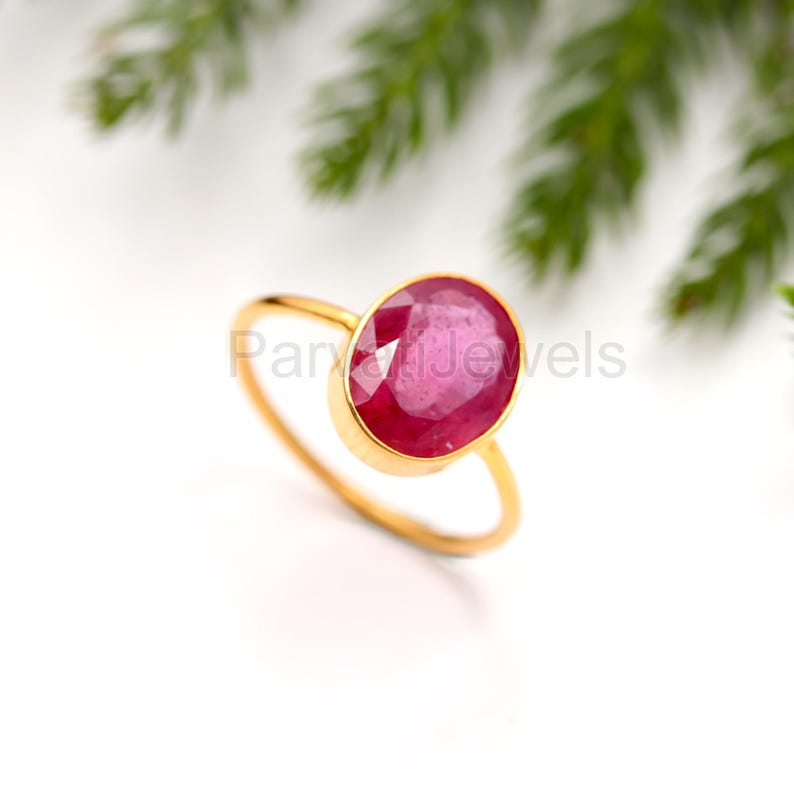 May include: A gold ring featuring a large, oval-shaped ruby gemstone. The ruby is a deep red colour and has a faceted cut.