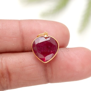 Puede incluir: Un colgante de corazón de oro con una piedra preciosa de rubí rojo.