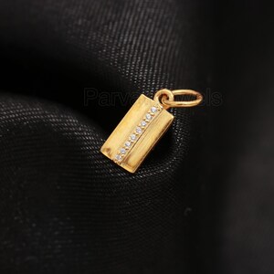 Puede incluir: Un colgante de oro con forma rectangular y una fila de peque&ntilde;as piedras transparentes.