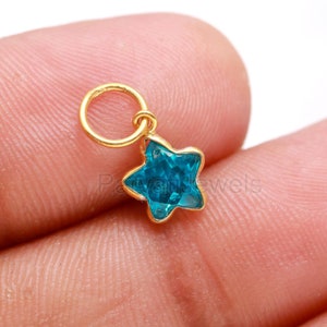 May include: Gold charm with a blue star-shaped crystal. The charm has a small loop at the top for attaching to a necklace or bracelet.