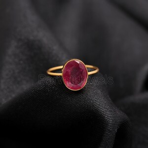 May include: A gold ring featuring a large, oval-shaped, red gemstone.